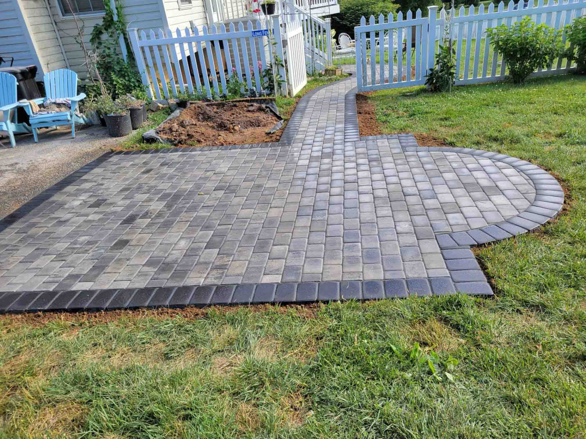 Paver walkway and patio in a backyard leading to the back door past a white picket fence