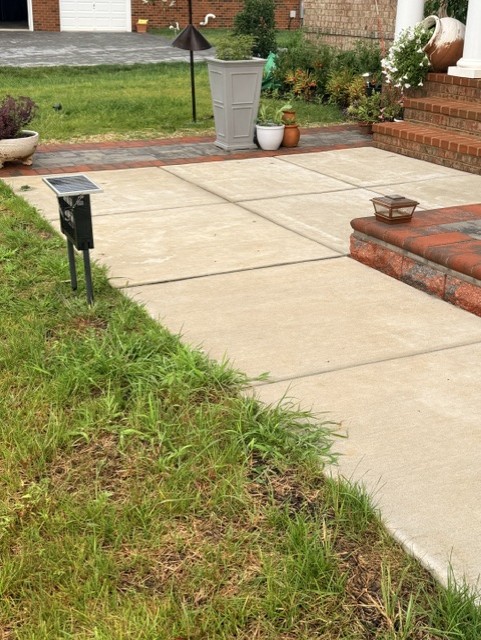 Concrete walkway edged with a paver border and brick step landing along the front of a home