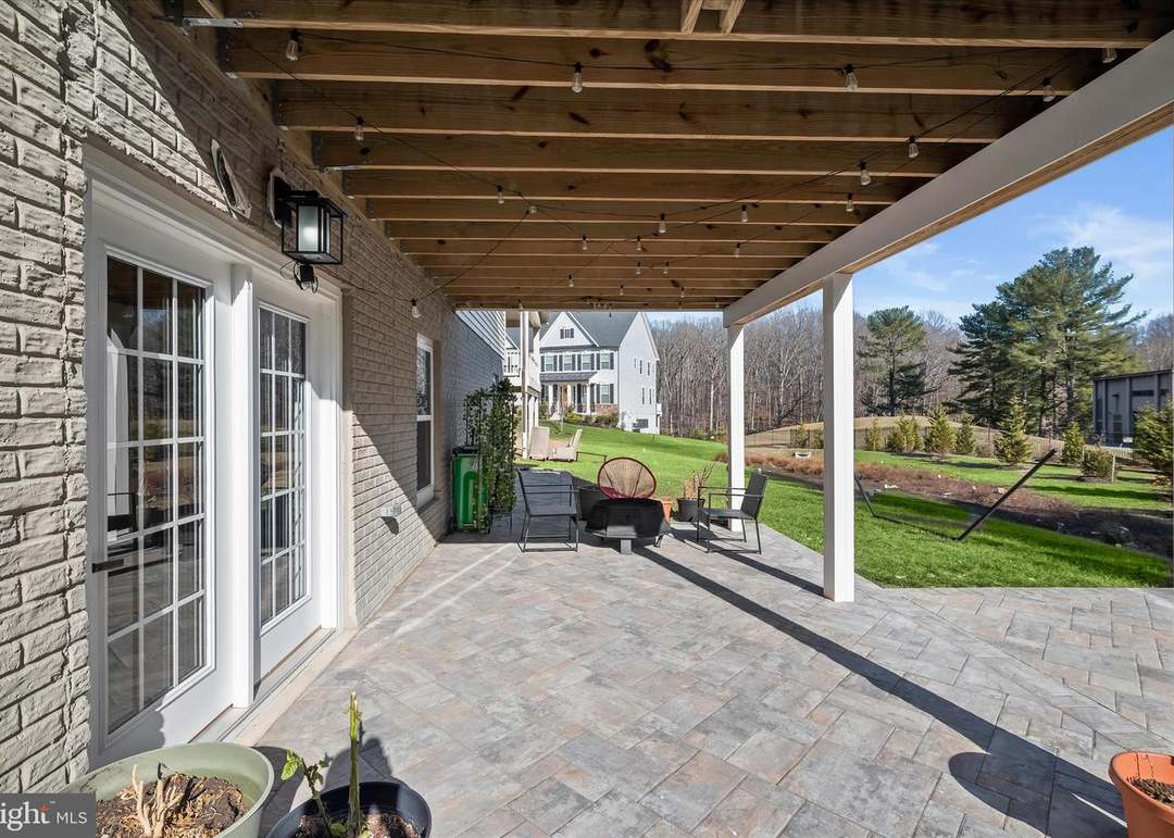 Large under-deck paver patio with fire pit and string lights beside a brick home